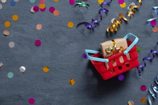 Shopping basket and festive tinsel flat lay on dark background. Top view.