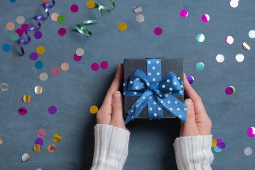 Female hands with a gift and festive tinsel flat lay on a dark cement background