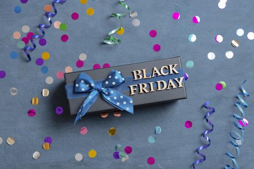 Black Friday text with gift and festive tinsel flat lay on dark cement background.