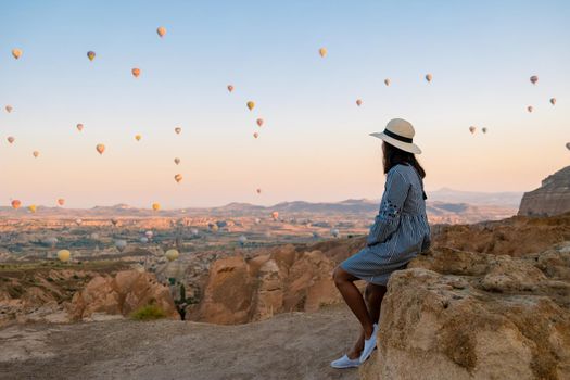 Asian women watching the sunset in Cappadocia with hot air balloons in the sky during sunrise in Cappadocia Turkey. Kapadokya Gorem. Happy mid age women in a hot air balloon