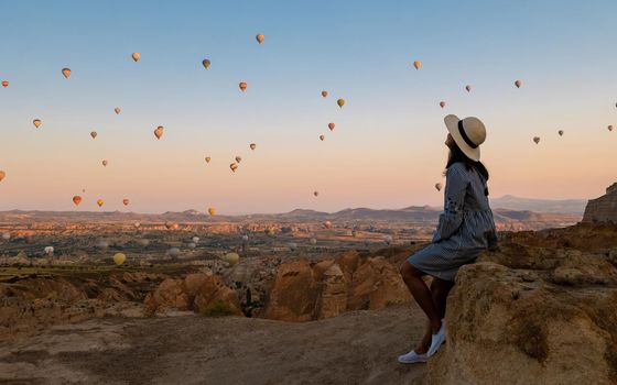 Asian women watching the sunset in Cappadocia with hot air balloons in the sky during sunrise in Cappadocia Turkey. Kapadokya Gorem. Happy mid age women in a hot air balloon