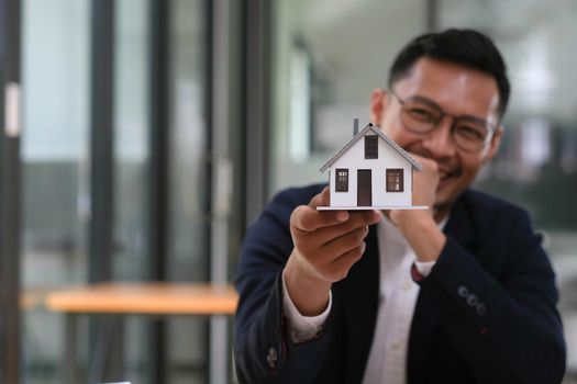 Business man hands holding modern house, House model with agent and customer discussing for contract to buy, get insurance or loan mortgage crisis real estate or property..