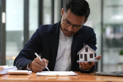 Business man hands holding modern house, House model with agent and customer discussing for contract to buy, get insurance or loan mortgage crisis real estate or property..