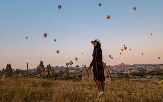 Asian women watching the sunset in Cappadocia with hot air balloons in the sky during sunrise in Cappadocia Turkey. Kapadokya Gorem. Happy mid age women in a hot air balloon