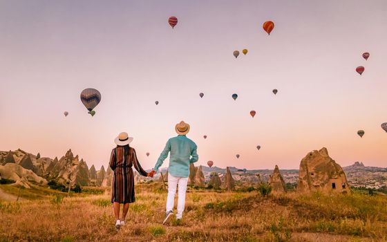 Asian women and caucasian men mid age on a trip to Kapadokya Cappadocia Turkey, a happy young couple during sunrise watching the hot air balloons of Kapadokya Cappadocia Turkey during vacation