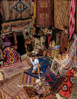 young man tourist at an old traditional Turkish carpet shop in cave house Cappadocia, Turkey Kapadokya. Colorful carpet shop in Goreme