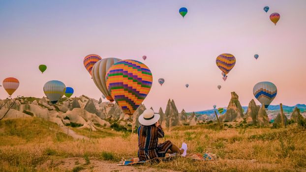 Asian women watching the sunset in Cappadocia with hot air balloons in the sky during sunrise in Cappadocia Turkey. Kapadokya Gorem. Happy mid age women in a hot air balloon