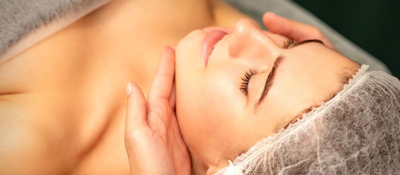 Facial massage. Hands of a masseur massaging neck of a young caucasian woman in a spa salon, the concept of health massage