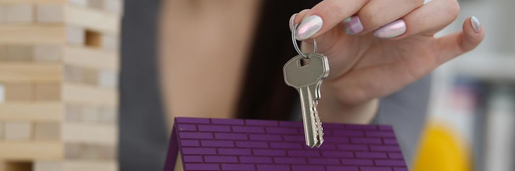 Close-up of female worker hand hold key to unlock new miniature toy house, buy new accommodation, invest in real estate. Agency, mortgage, realtor concept