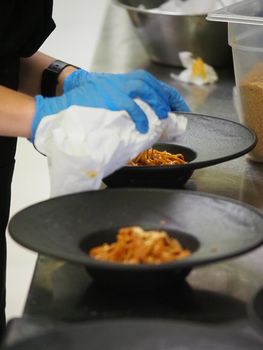 closeup of a chef hand wearing gloves serving and decorating a plate of pasta