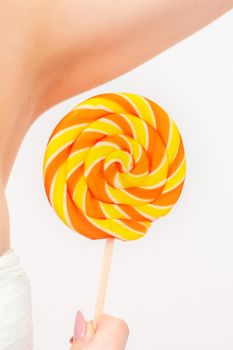 Waxing, depilation concept. A young female holds a round lollipop near her armpit on white background