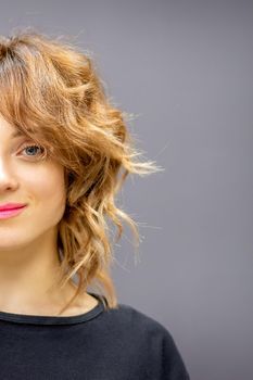 Portrait of a beautiful young caucasian red-haired woman with short wavy hairstyle smiling and looking at camera on dark gray background with copy space