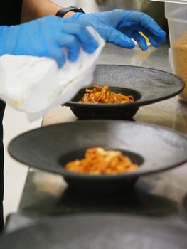 closeup of a chef hand wearing gloves serving and decorating a plate of pasta