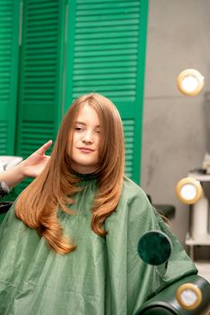 Professional hair care. Young female red-haired with long hair receiving hairstyling in a beauty salon.