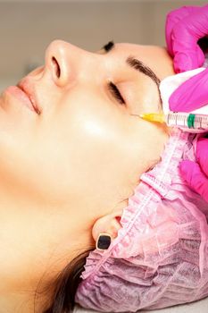 The young white woman is getting rejuvenating facial injections with hyaluronic acid on the eye in a beauty clinic