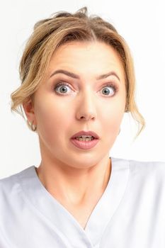 Female doctor shocked. Close up portrait of a young caucasian woman looking surprised with wide eyes stared isolated white wall background