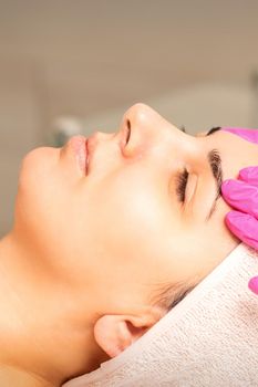 Cosmetologist with gloved hands applies a moisturizing mask with peeling cream on the female face. Facial cosmetology treatment. Procedures for facial care