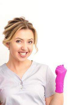 Happy caucasian woman doctor wearing pink gloves celebrates and raising fists on white background