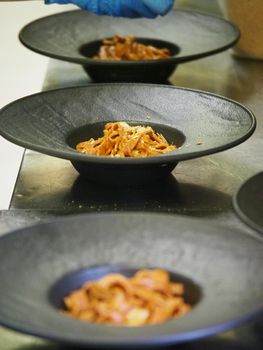 closeup of a chef hand wearing gloves serving and decorating a plate of pasta