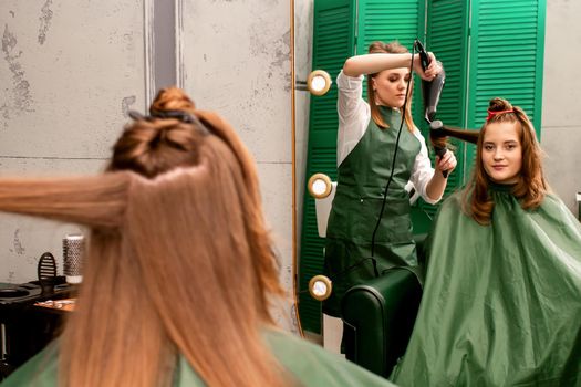 The hairdresser is drying long brown hair with a hairdryer and round brush in a beauty salon