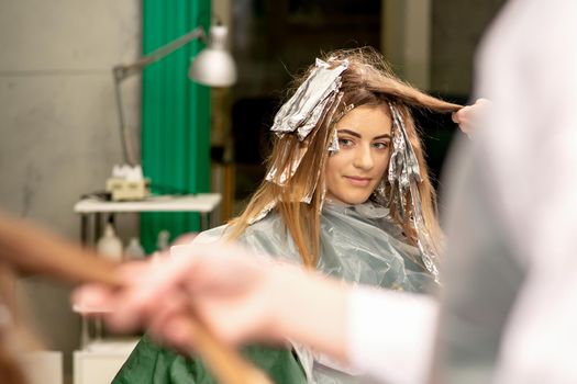 Portrait of a beautiful young caucasian woman who is smiling getting dyeing her hair with foil in a beauty salon