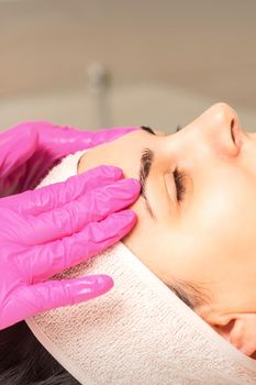 Cosmetologist with gloved hands applies a moisturizing mask with peeling cream on the female face. Facial cosmetology treatment. Procedures for facial care