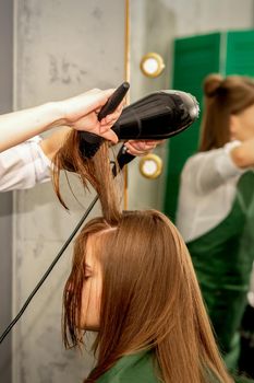 The hairdresser is drying long brown hair with a hairdryer and round brush in a beauty salon