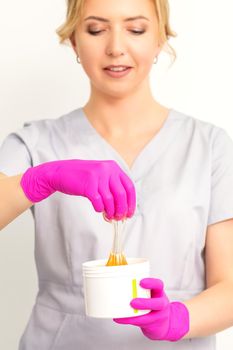 Portrait of a female caucasian beautician holding a jar of sugar paste for sugaring wearing pink gloves on white background