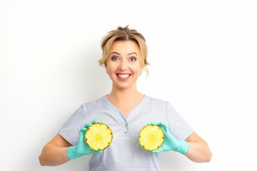 Young Caucasian smiling woman doctor nutritionist holding slices pineapple over isolated white background, breast health concept