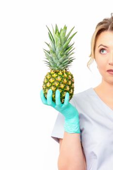 Young caucasian female doctor nutritionist holding fresh pineapple over white background