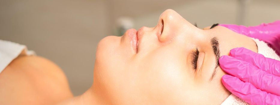 Cosmetologist with gloved hands applies a moisturizing mask with peeling cream on the female face. Facial cosmetology treatment. Procedures for facial care