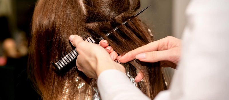 Hairdresser's hands prepare brown hair for dyeing with a comb and foil in a beauty salon, close up