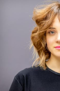 Portrait of a beautiful young caucasian red-haired woman with short wavy hairstyle smiling and looking at camera on dark gray background with copy space