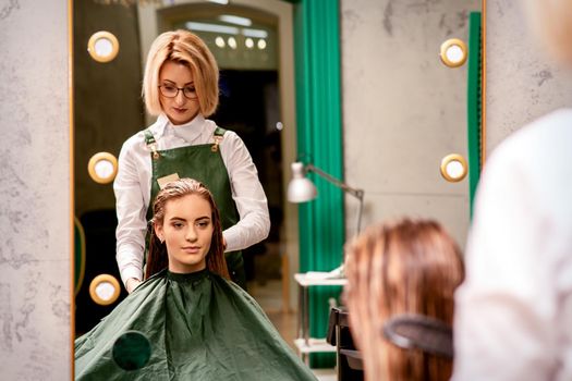 Professional hair care. Beautiful young caucasian brunette woman with long hair receiving hairstyling in a beauty salon