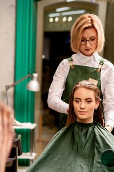 Professional hair care. Beautiful young caucasian brunette woman with long hair receiving hairstyling in a beauty salon