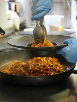closeup of a chef hand wearing gloves serving and decorating a plate of pasta