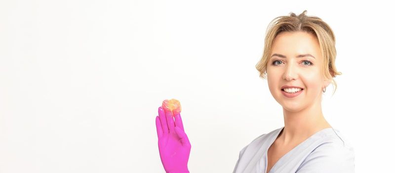 Young caucasian smiling female beautician holding wax for depilation over white background. Yellow sugar paste in hands master of depilation. Epilation concept