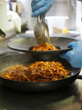 closeup of a chef hand wearing gloves serving and decorating a plate of pasta