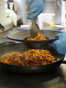 closeup of a chef hand wearing gloves serving and decorating a plate of pasta