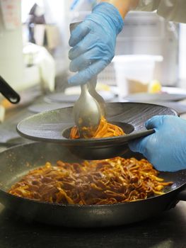 closeup of a chef hand wearing gloves serving and decorating a plate of pasta