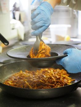 closeup of a chef hand wearing gloves serving and decorating a plate of pasta