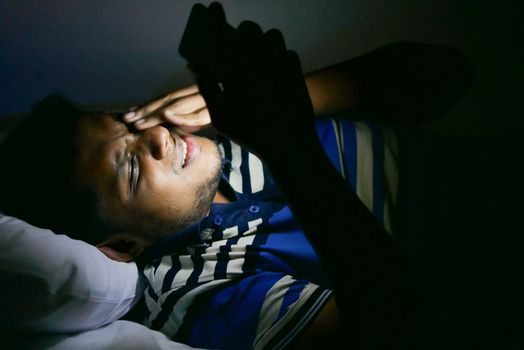 young man sitting on bed using smart phone at night .