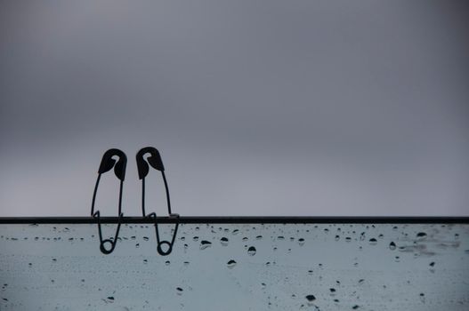 Safety pin couple sitting on glass wall with customizable space for text and ideas. Love and romance concept.