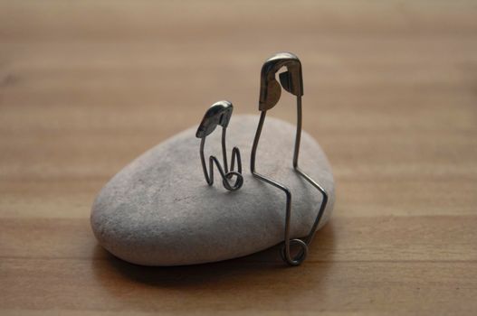 Model safety pin of parent and child sitting on a rock with customizable space for text or ideas. Family concept.