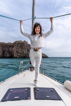 Woman standing on the nose of the yacht at a sunny summer day, breeze developing hair, beautiful sea on background.