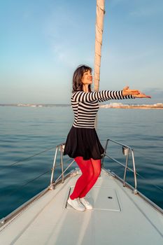 Woman standing on the nose of the yacht at a sunny summer day, breeze developing hair, beautiful sea on background.