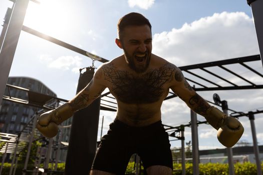 Man in boxing gloves is practicing on an outdoor sports field.