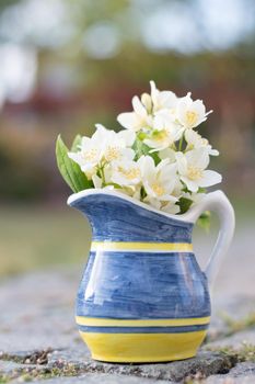 a beautiful mini bouquet of jasmine in a yellow-blue vase on a stone path in the garden, a peaceful still life,. High quality photo