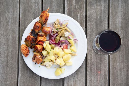summer picnic food, homemade chicken barbecue with vegetable salad and cold boiled potatoes, red wine in a glass, traditional belgian dish serving. High quality photo