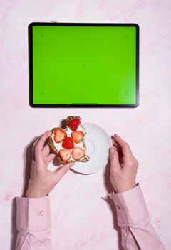 woman holding soft cheese and strawberry sandwich near green screen tablet, concept of healthy food and diet, using calorie counting app, top view, High quality photo
